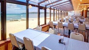 Un restaurante con mesas y sillas, amplias ventanas que dan a la playa y un interior de madera.
