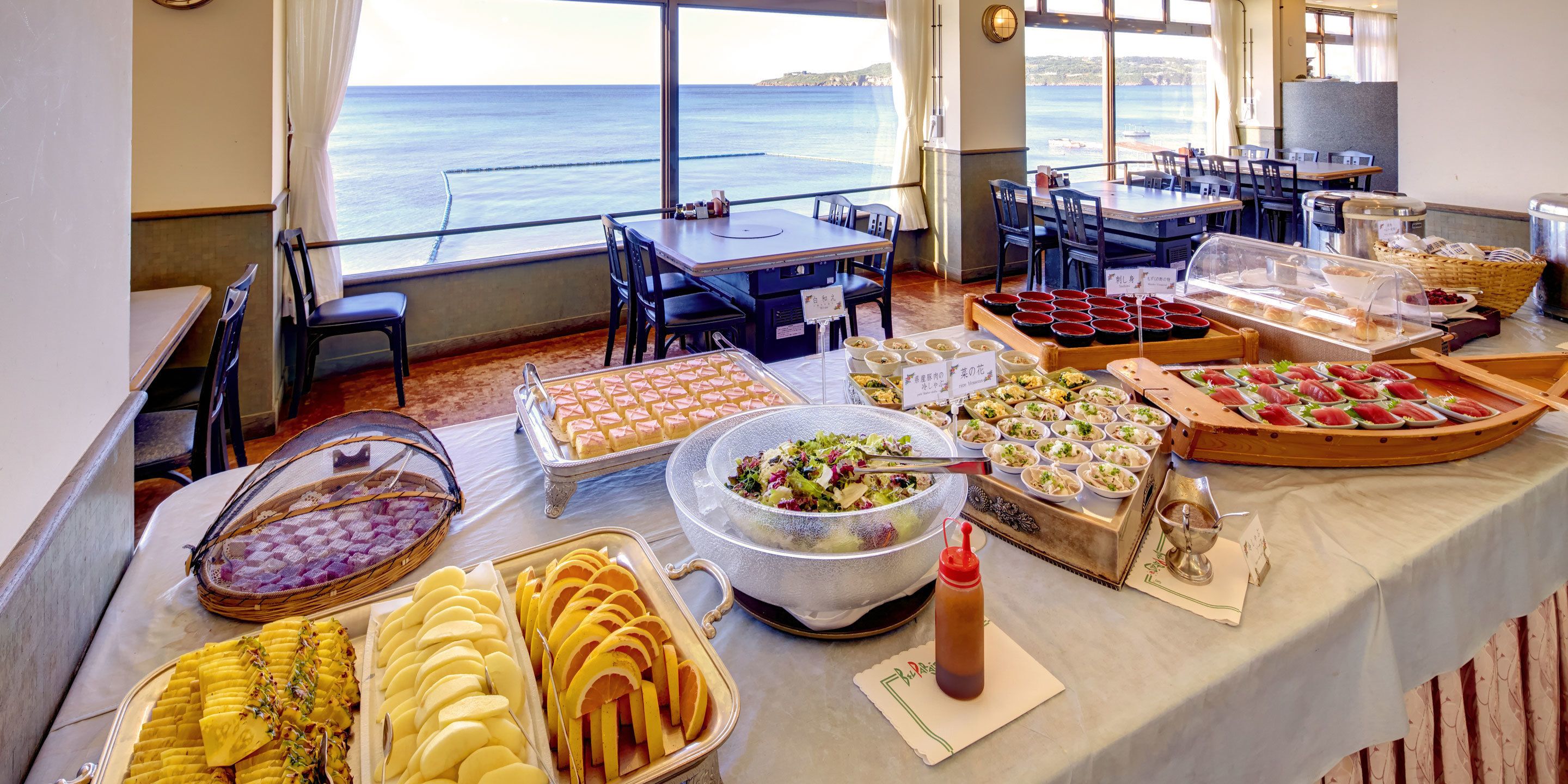 A buffet setup with various food items and a view of the sea.