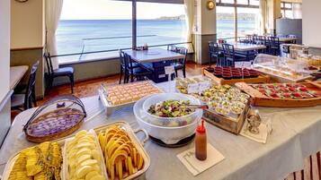A buffet setup with various food items and a view of the sea.