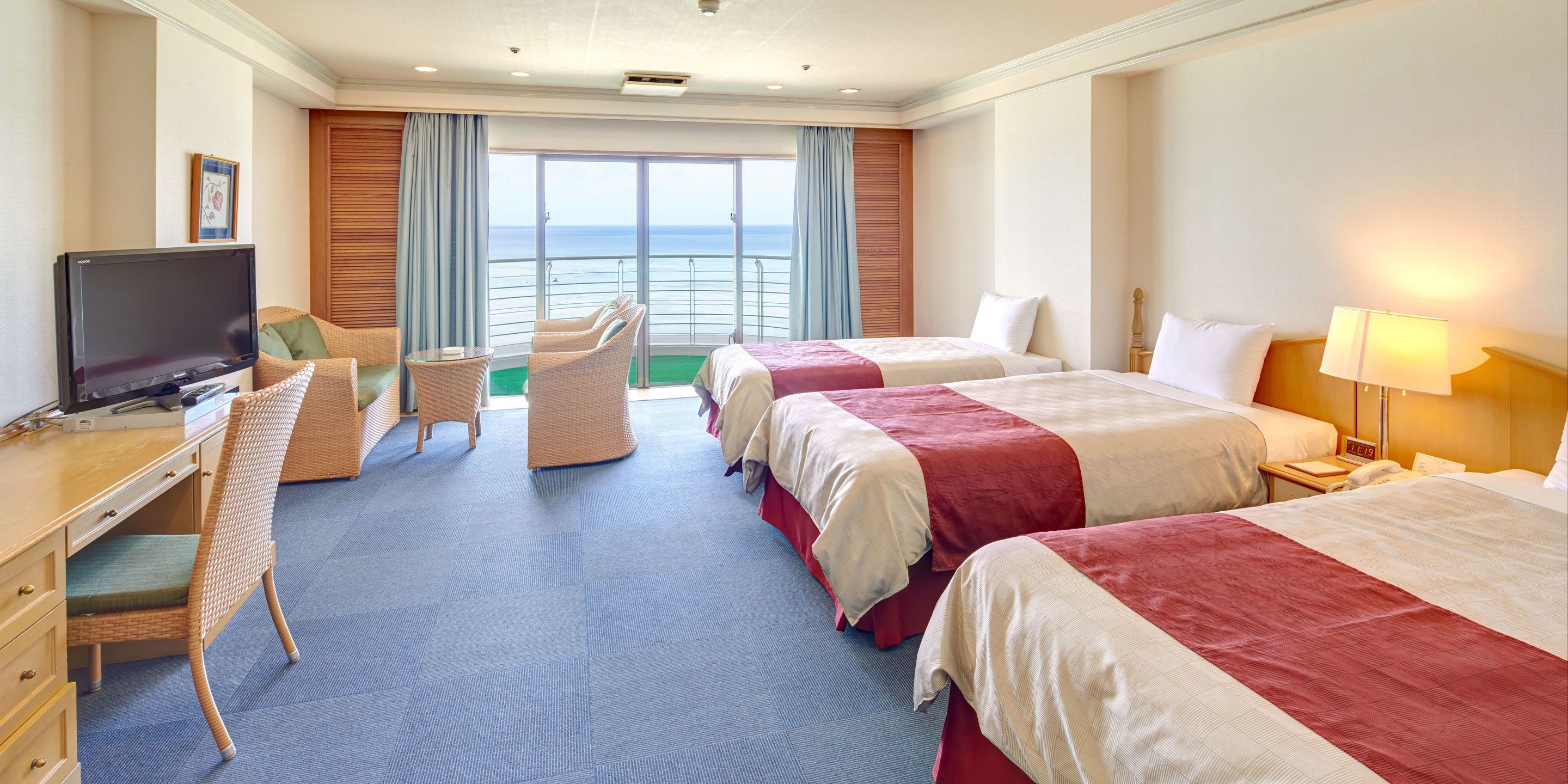 A hotel room with a large bed, a desk with a television, a chair, and a view of the ocean.