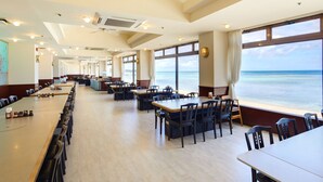 Un restaurante amplio con múltiples mesas y sillas, grandes ventanales con vistas al océano y una decoración de diseño moderno.