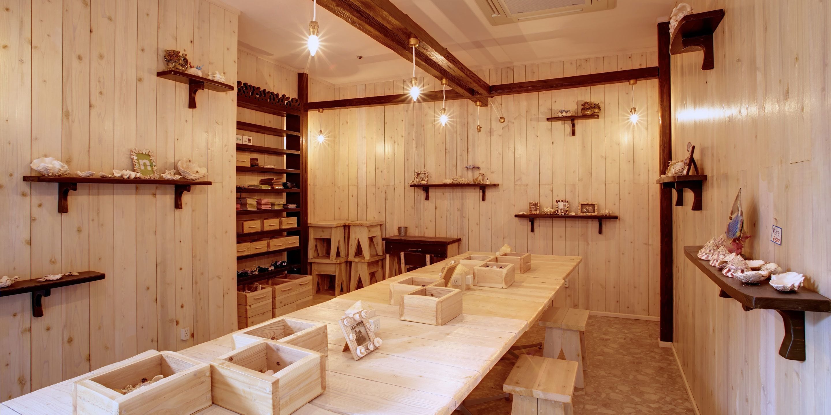 A wooden interior with a long table, shelves, and wooden stools.