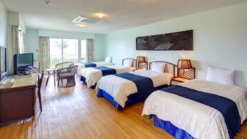 A hotel room with three beds, a desk with a television, and a large window.