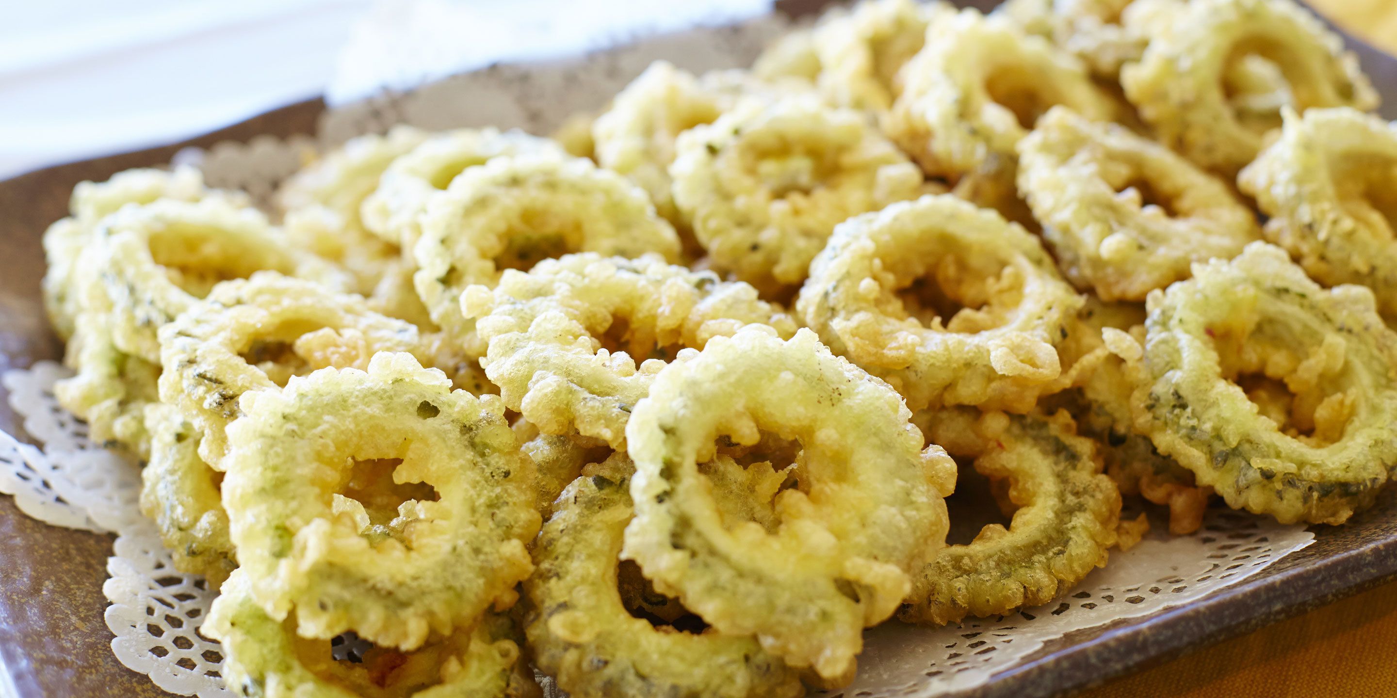 A tray of fried calamari rings on a ceramic plate with a lace doily underneath.