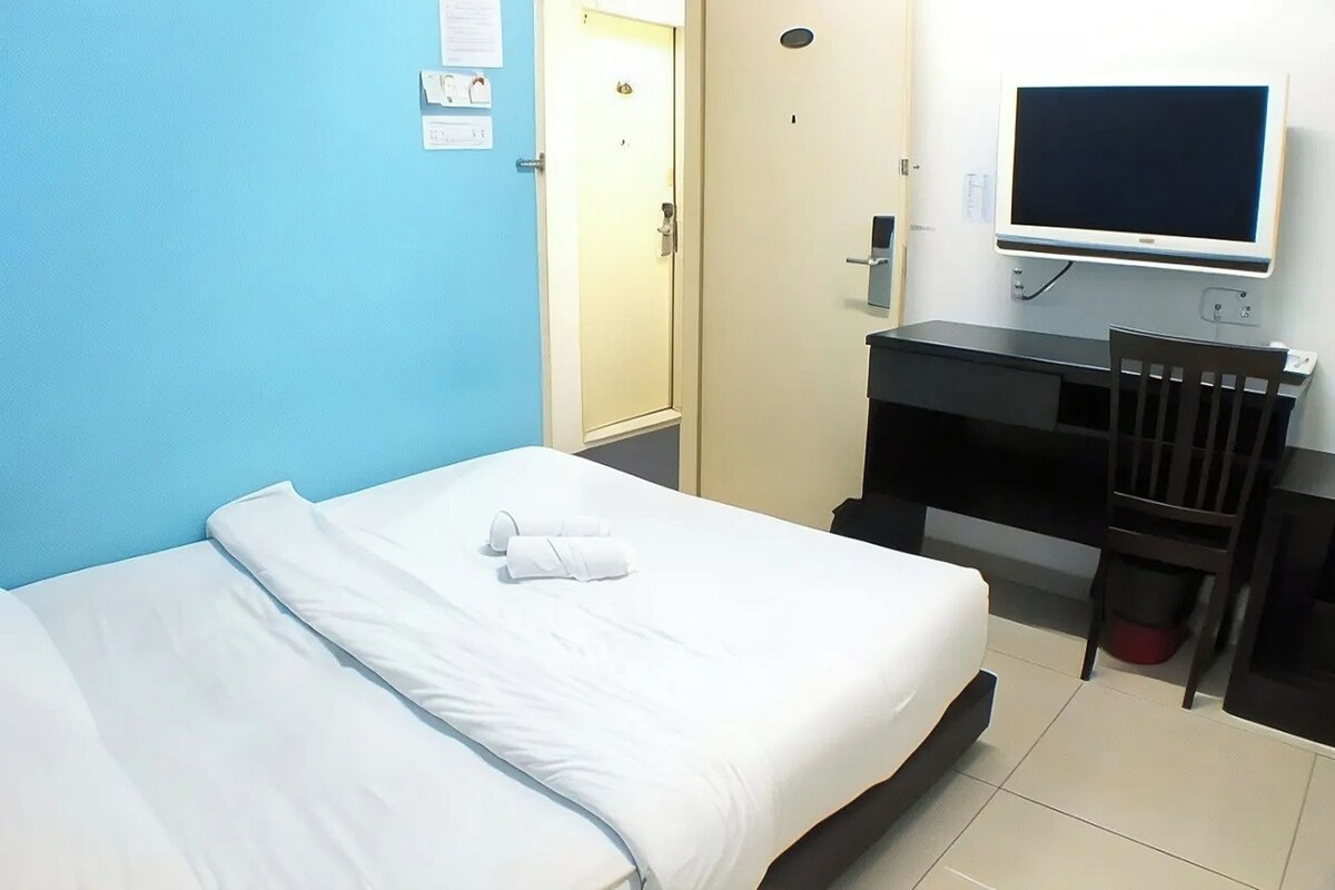 A hotel room with a bed, a desk, a chair, and a TV.
