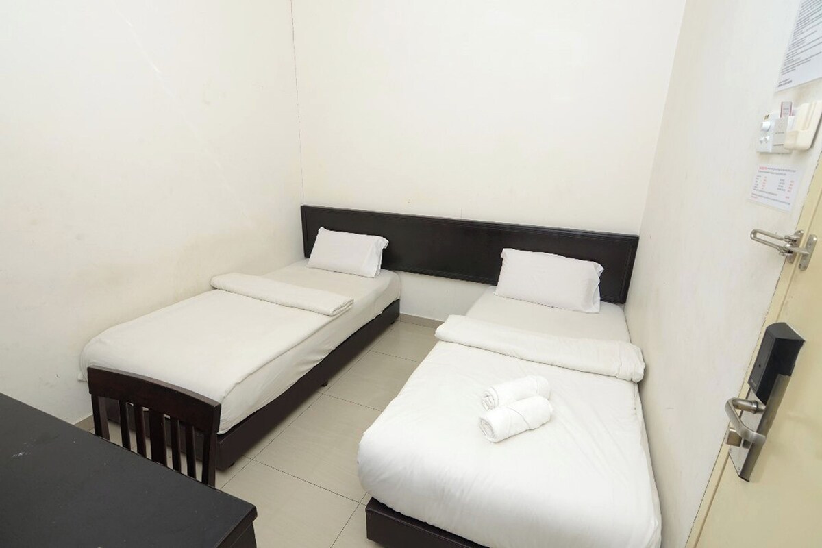 A small, clean room with two single beds, a wooden nightstand, and a door with a lock.
