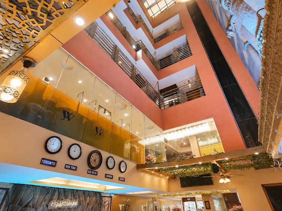 A multi-level atrium with a glass ceiling, clocks indicating different time zones, and a decorative ceiling with hanging plants.