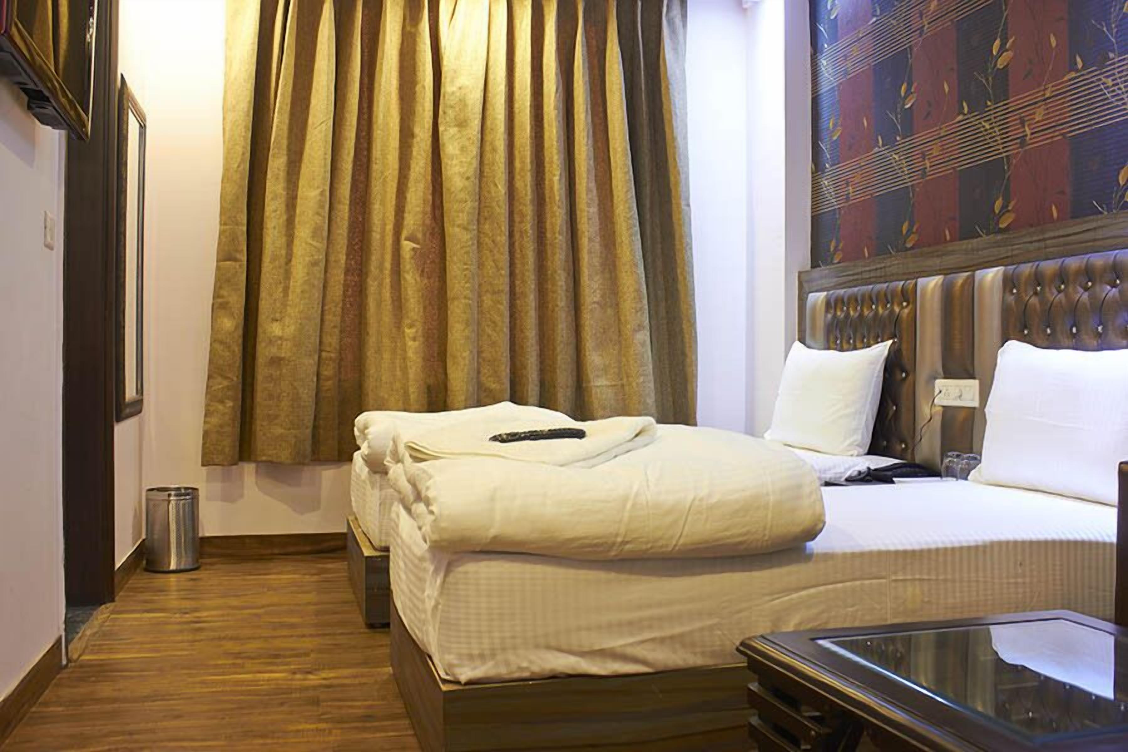 A hotel room with two beds, a wooden floor, a large window with curtains, and a wall-mounted television.