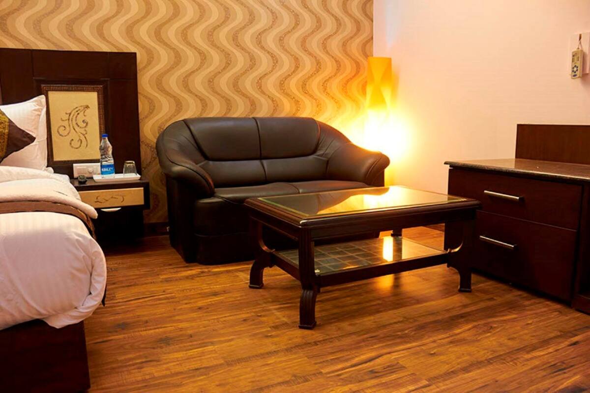 A hotel room with a bed, a leather sofa, a wooden coffee table, a nightstand with a lamp, and a dresser.