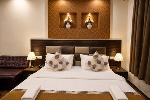 A hotel room with a large bed, two bedside lamps, a brown leather sofa, and a decorative wall with two vases. - Hotel Waterfall (New Delhi)
