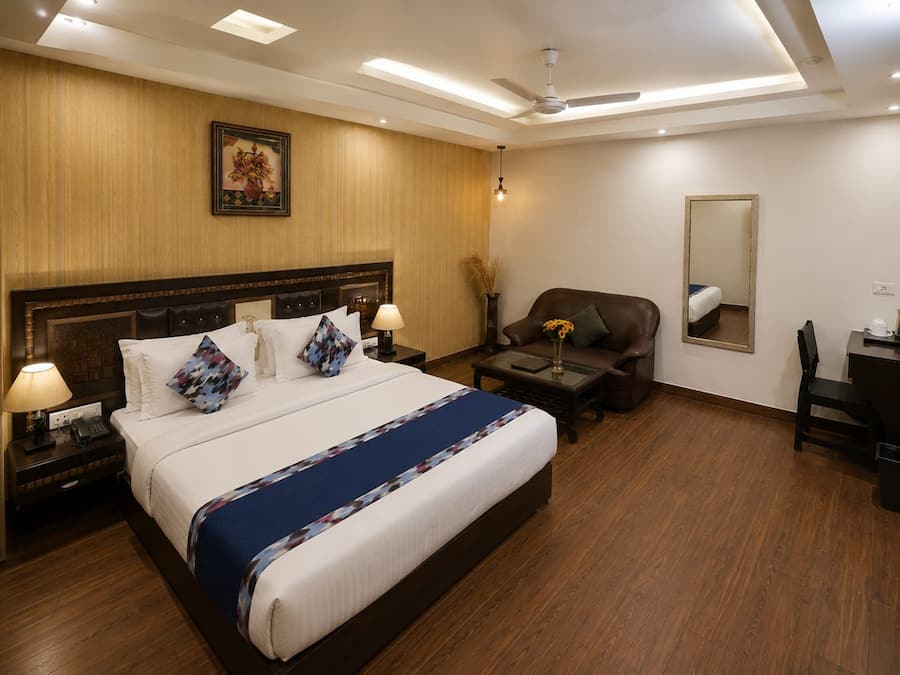 A hotel room with a large bed, bedside tables, a desk, a chair, a mirror, and a ceiling fan.