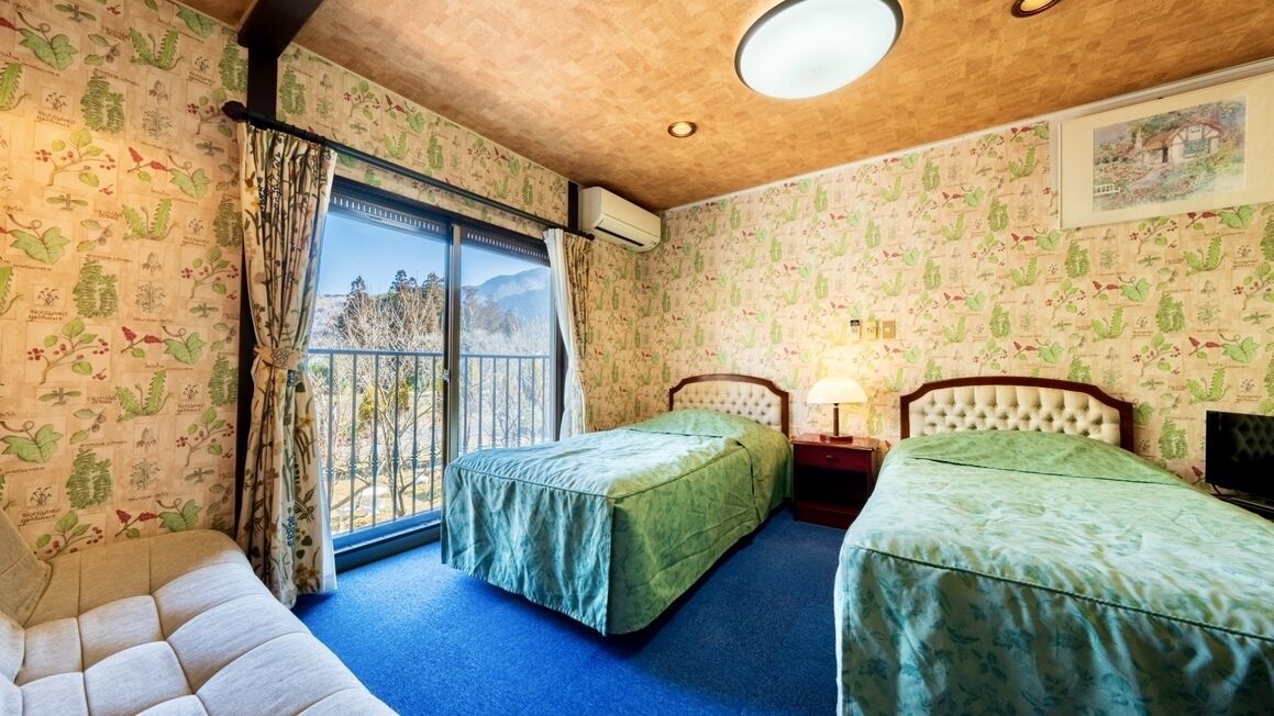 Una habitación con dos camas, una ventana con cortinas, una lámpara en el techo y un aire acondicionado instalado en la pared.