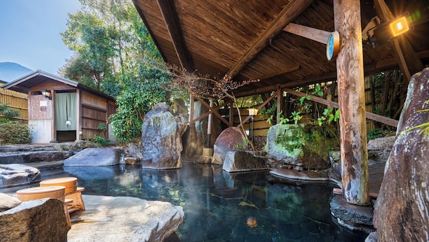 A traditional wooden structure with a stone bath surrounded by rocks and greenery. - Pension Yufuin (Yufu)