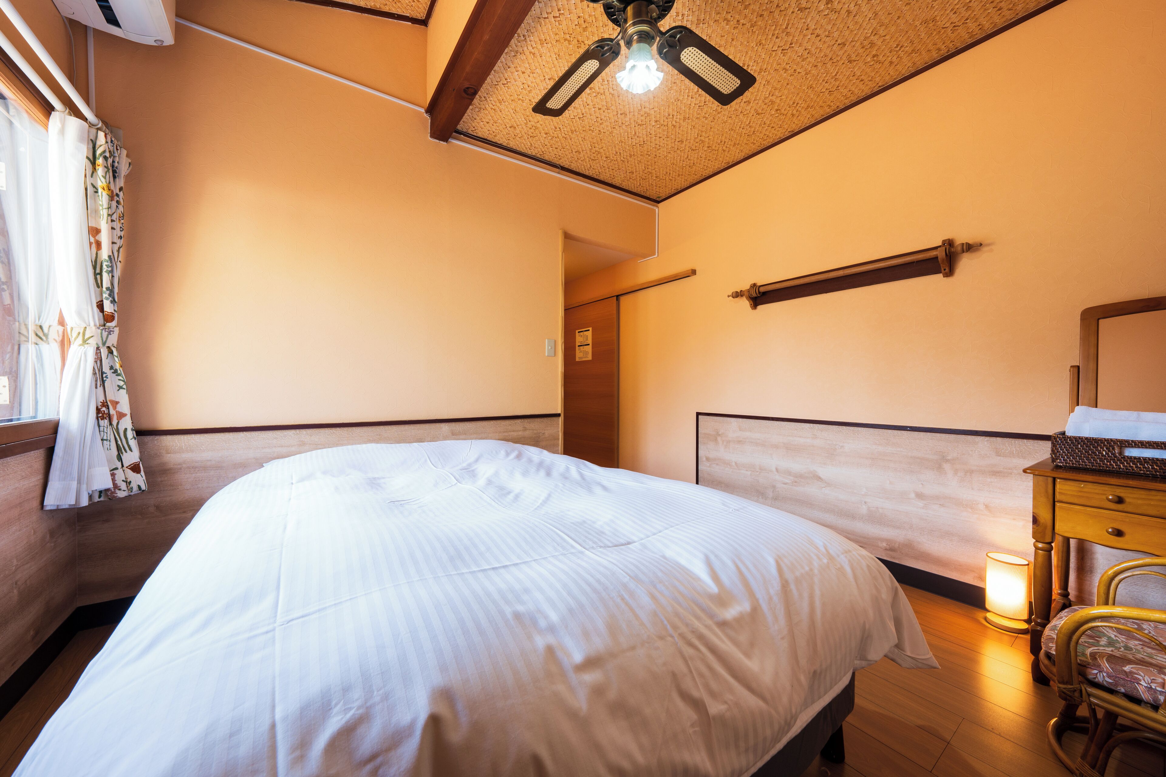 A hotel room with a large bed, wooden headboard, a ceiling fan, a nightstand, and a mirror.