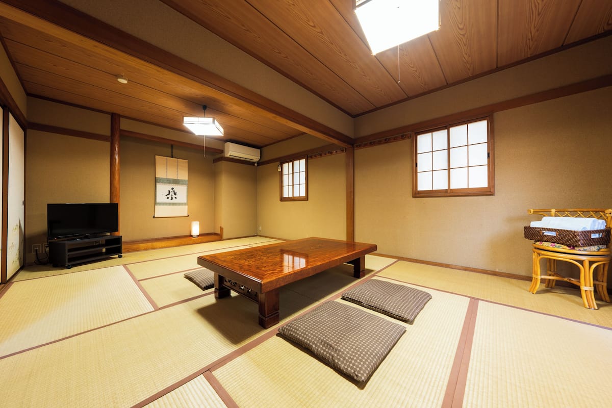Una habitación con tatamis, una mesa de madera, un televisor y un divisor de ambientes japonés tradicional.