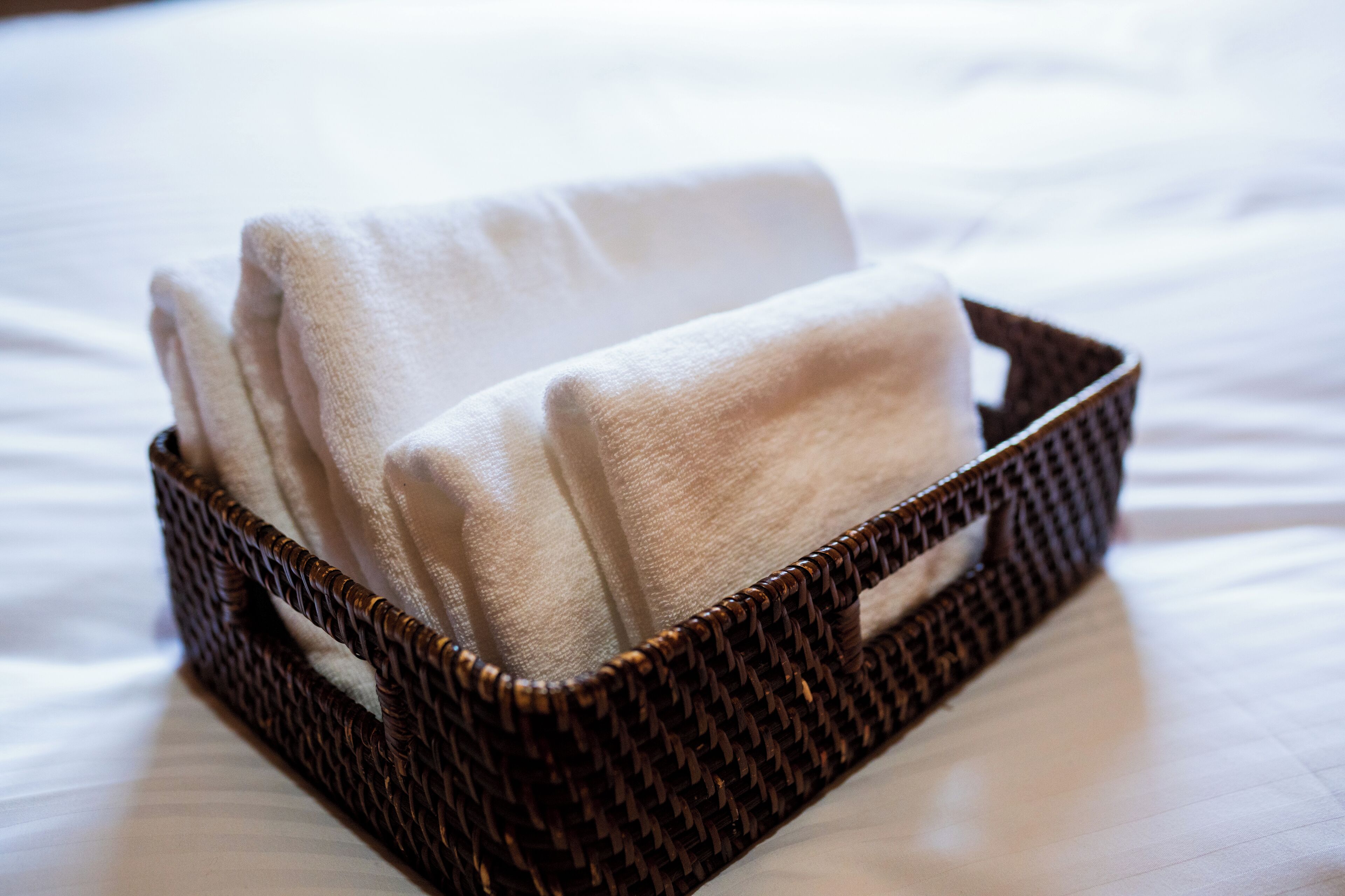 A wicker basket containing folded towels on a bed.