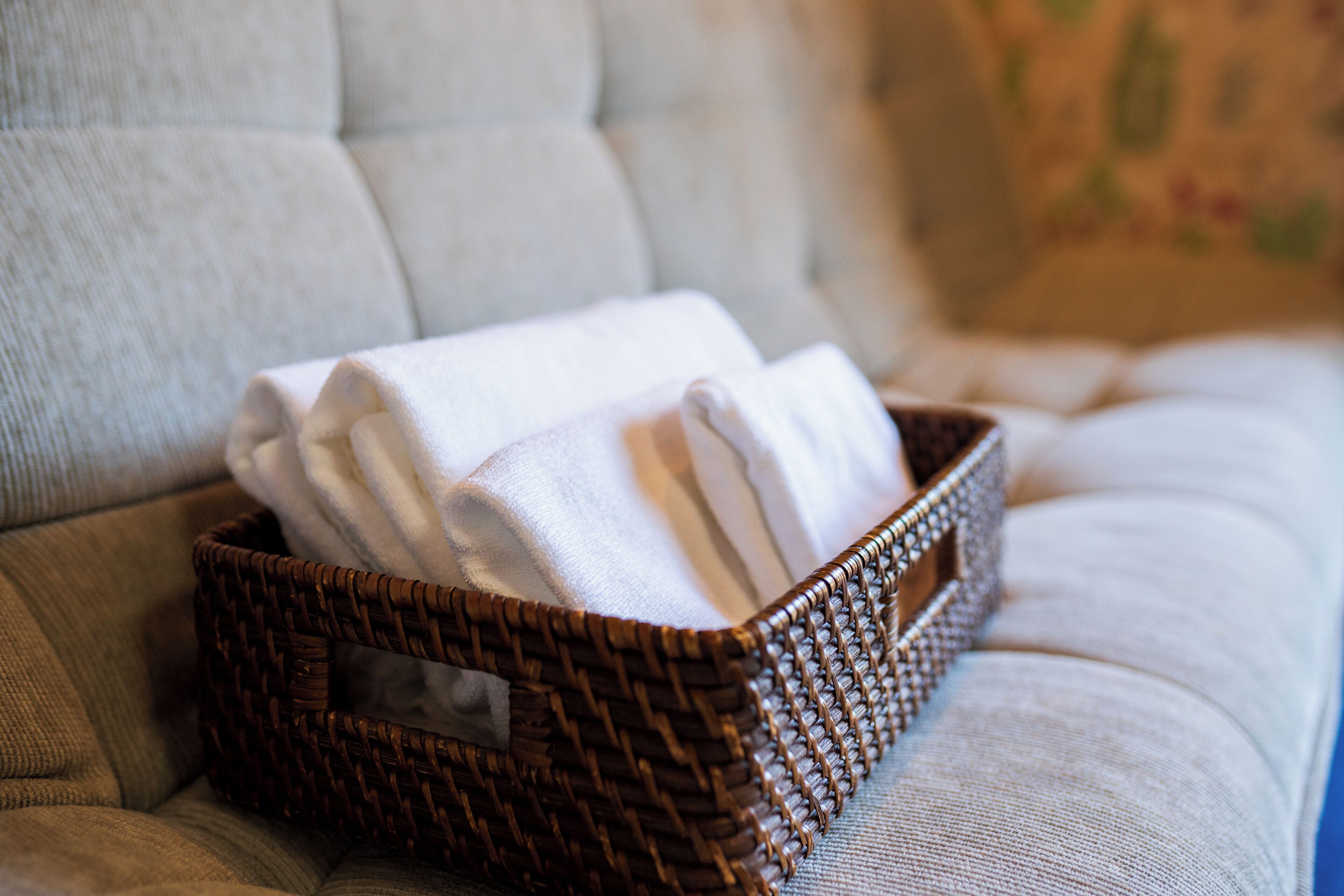 A wicker basket with folded towels on a cushioned surface.