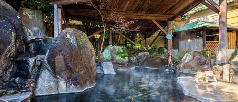 Uma onsen japonesa tradicional com estrutura de madeira, pedras grandes e uma fonte termal cristalina.