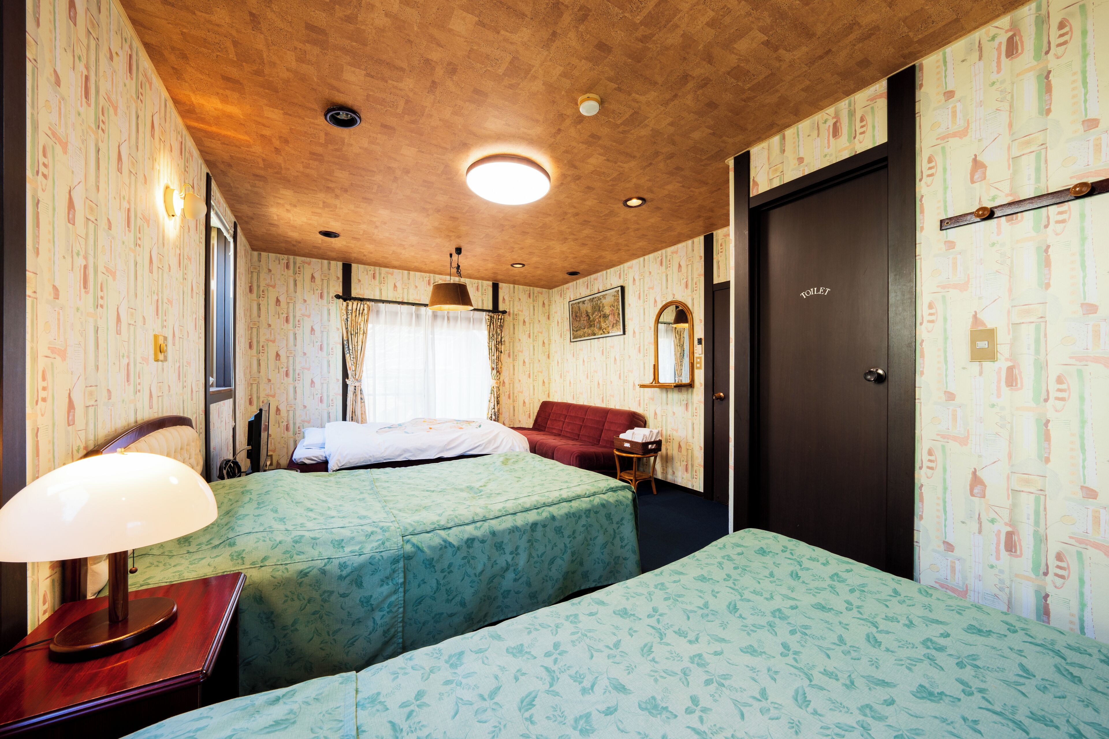 A hotel room with two beds, a wooden ceiling, a mirror, and a door labeled "TOILET".