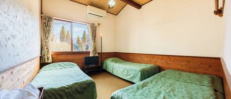 Una habitación con dos camas individuales, un ventilador de techo, una ventana con cortinas y una mesita de noche con lámpara.