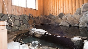 A wooden cabin interior with a stone-walled hot tub and a window. - Pension Yufuin (Yufu)