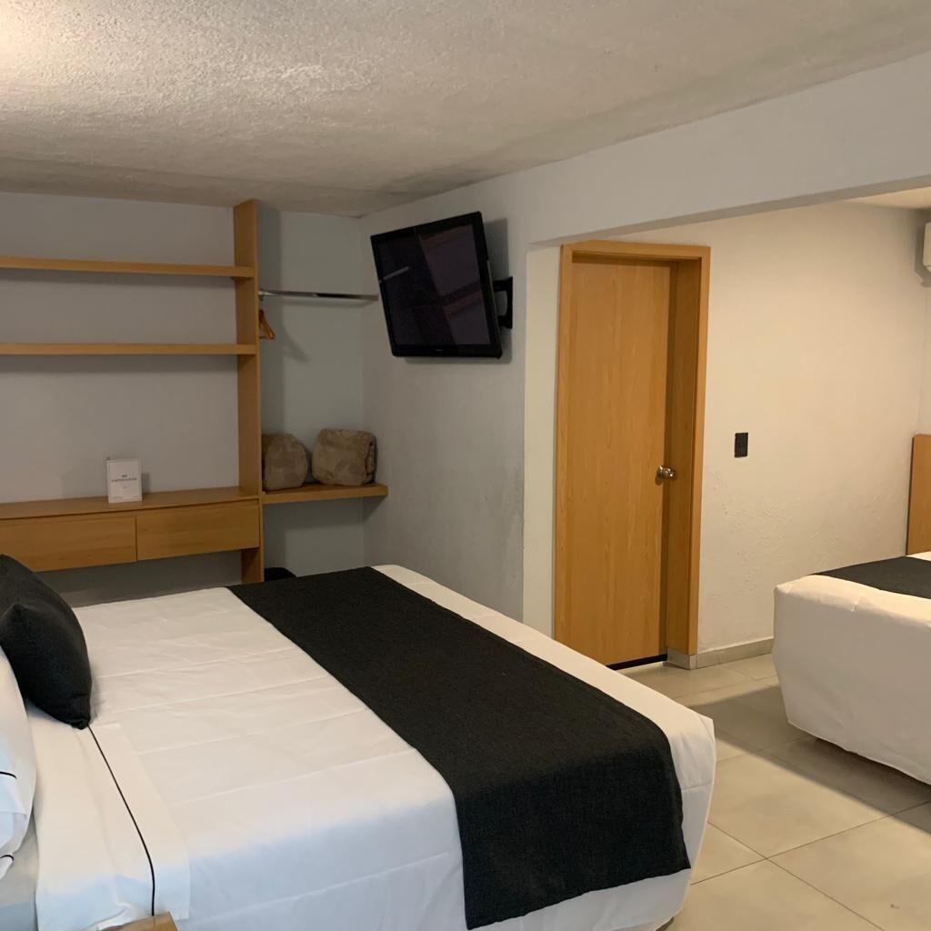 Een hotelkamer met twee bedden, een aan de muur bevestigde televisie, een houten deur en een plank met een tas en een doos.