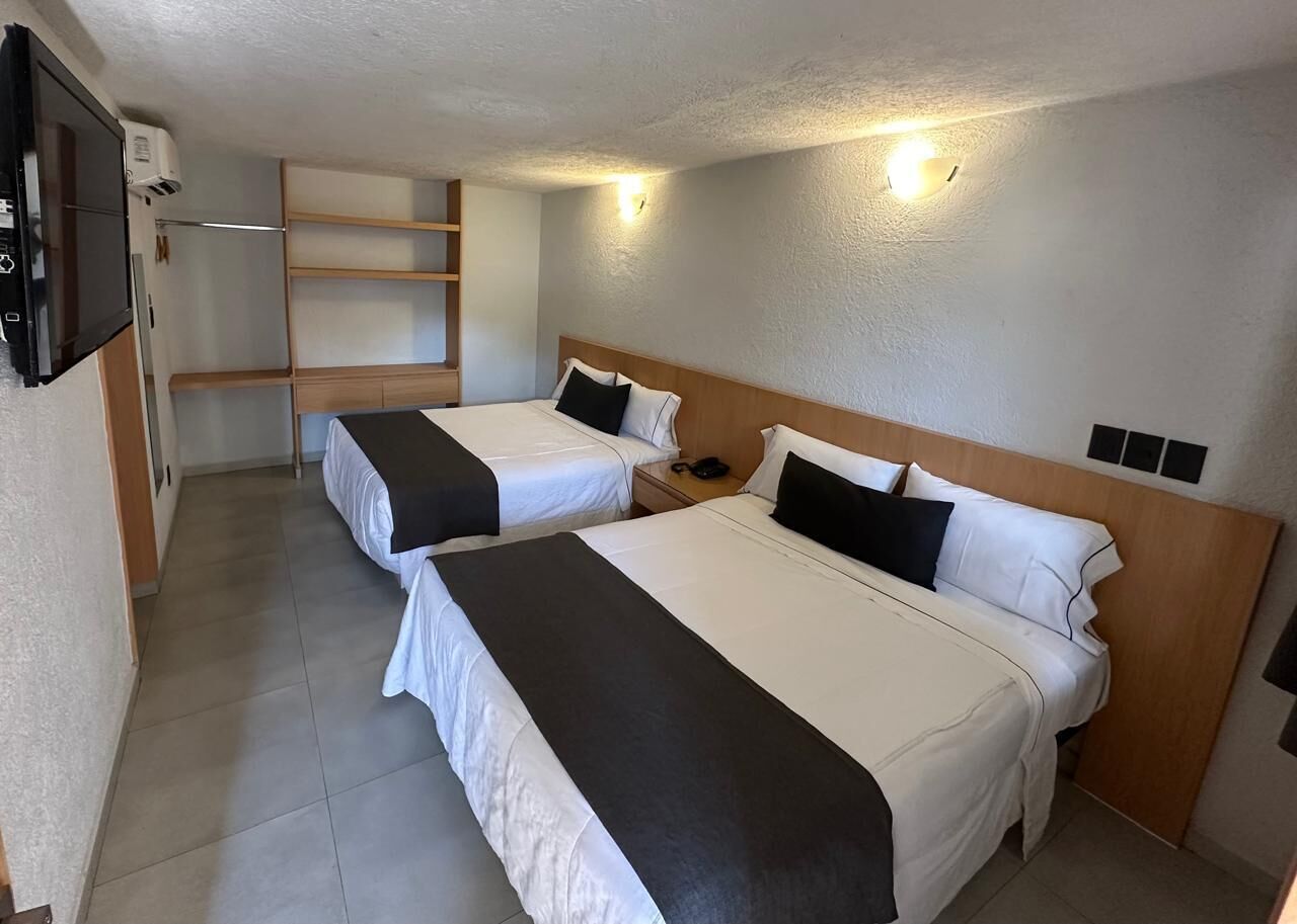 A hotel room with two beds, a TV, a phone, and a shelf unit.