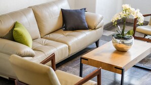 A modern living room with a beige leather sofa, a wooden coffee table, and a chair. There is a potted orchid on the table. - Hotel Emperador Centro Guadalajara y Remodelado (Guadalajara)