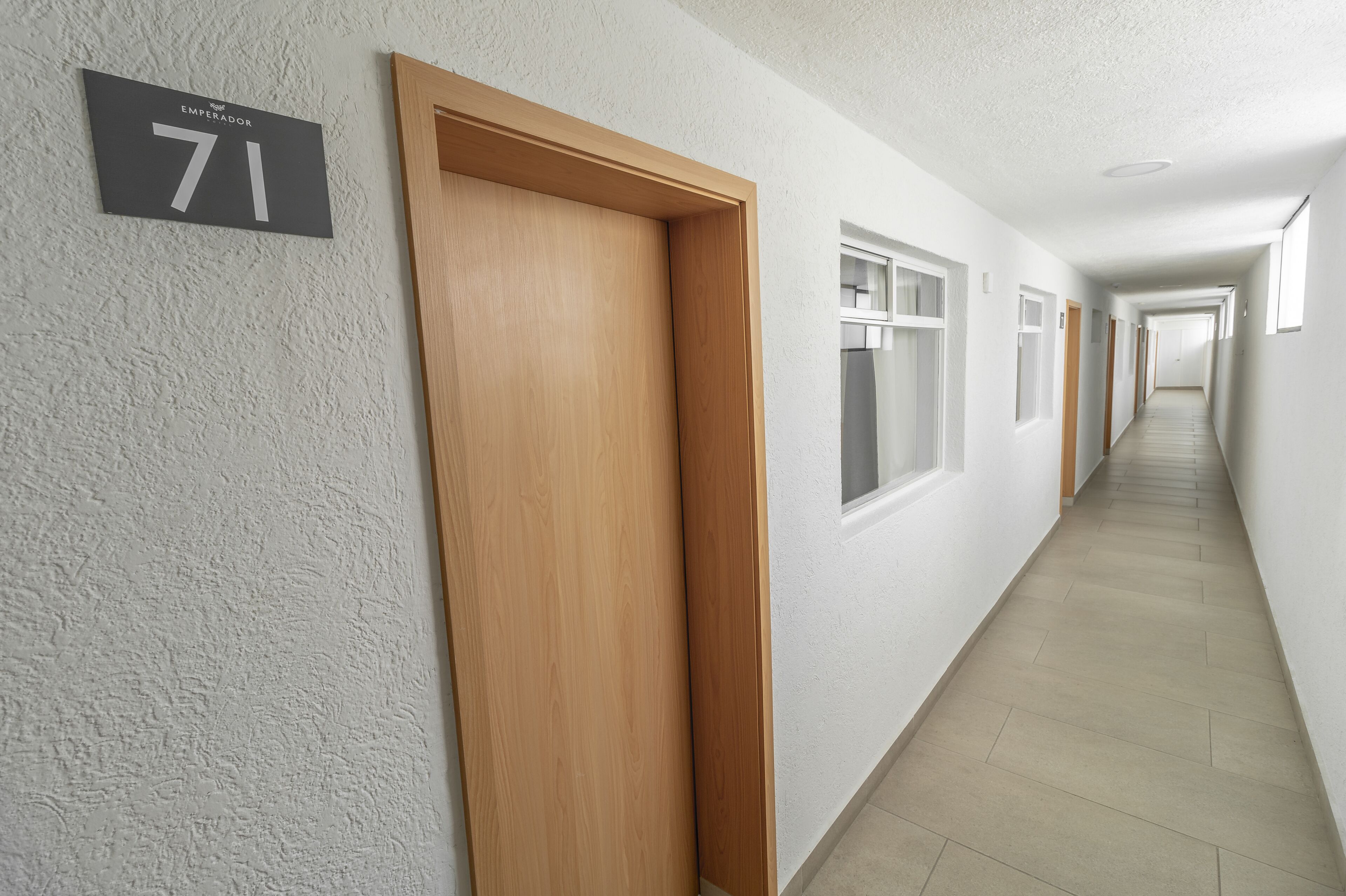 A hallway with a number sign '71' on the wall, wooden doors, and a tiled floor.