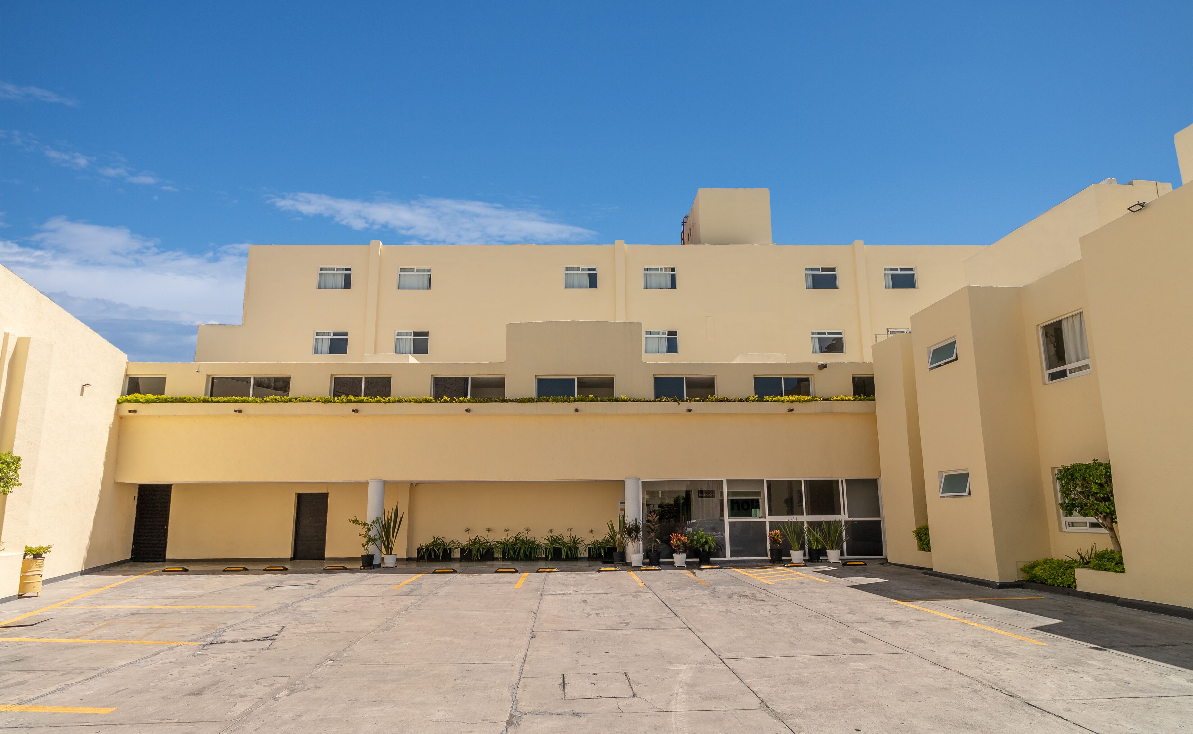 A multi-story building with a flat facade, a central entrance, and a parking area with marked spaces.