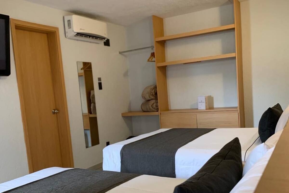 Una habitación con dos camas, un armario de madera, un espejo y un estante con toallas dobladas.