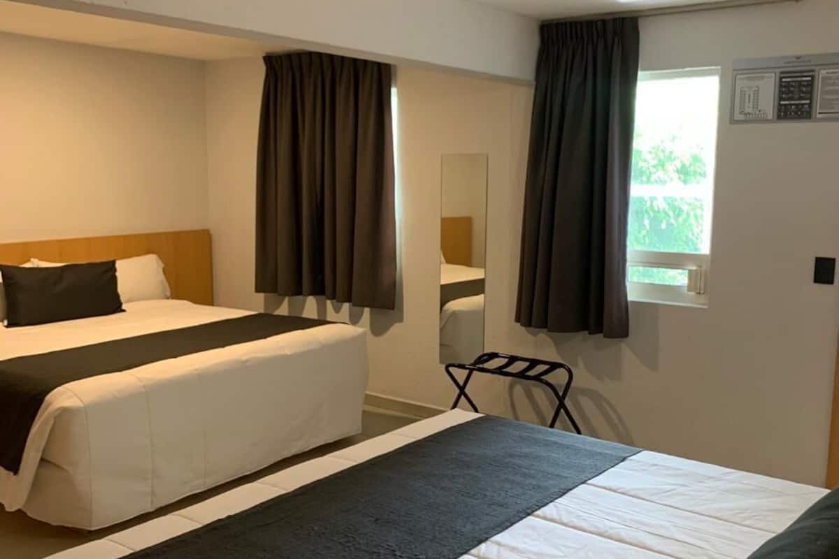 Habitación de hotel con dos camas, un espejo grande y una ventana con cortinas.