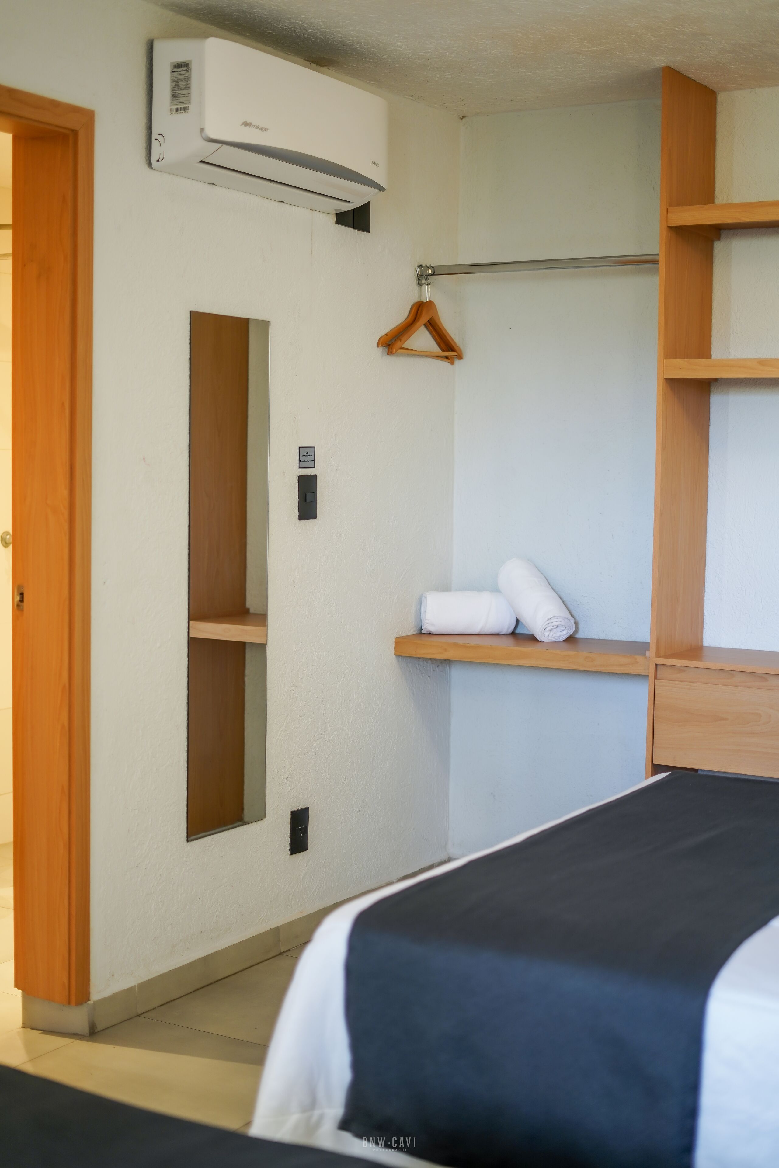 Quarto de hotel com cama, guarda-roupa de madeira, cabideiro e unidade de ar condicionado na parede.