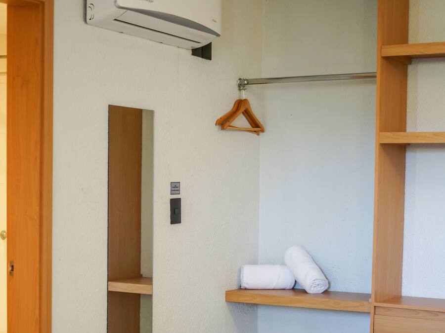 Quarto de hotel com cama, guarda-roupa de madeira, cabideiro e unidade de ar condicionado na parede.