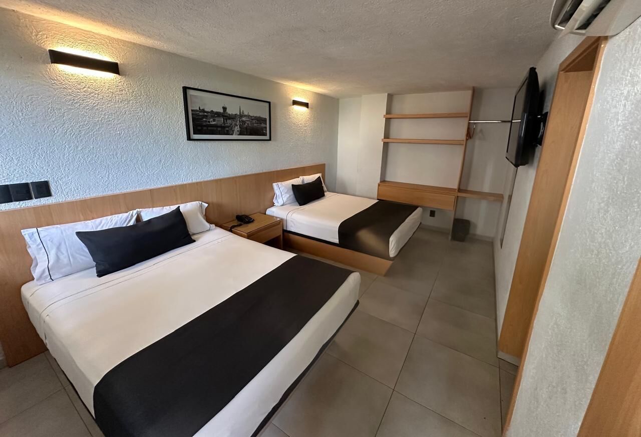 A hotel room with two beds, a flat-screen TV, and a framed picture on the wall.