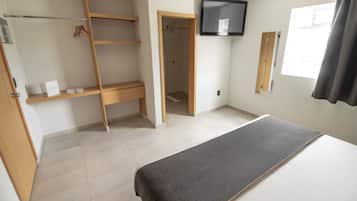 Un dormitorio con cama, un armario de madera, zona de ducha y televisor montado en la pared.