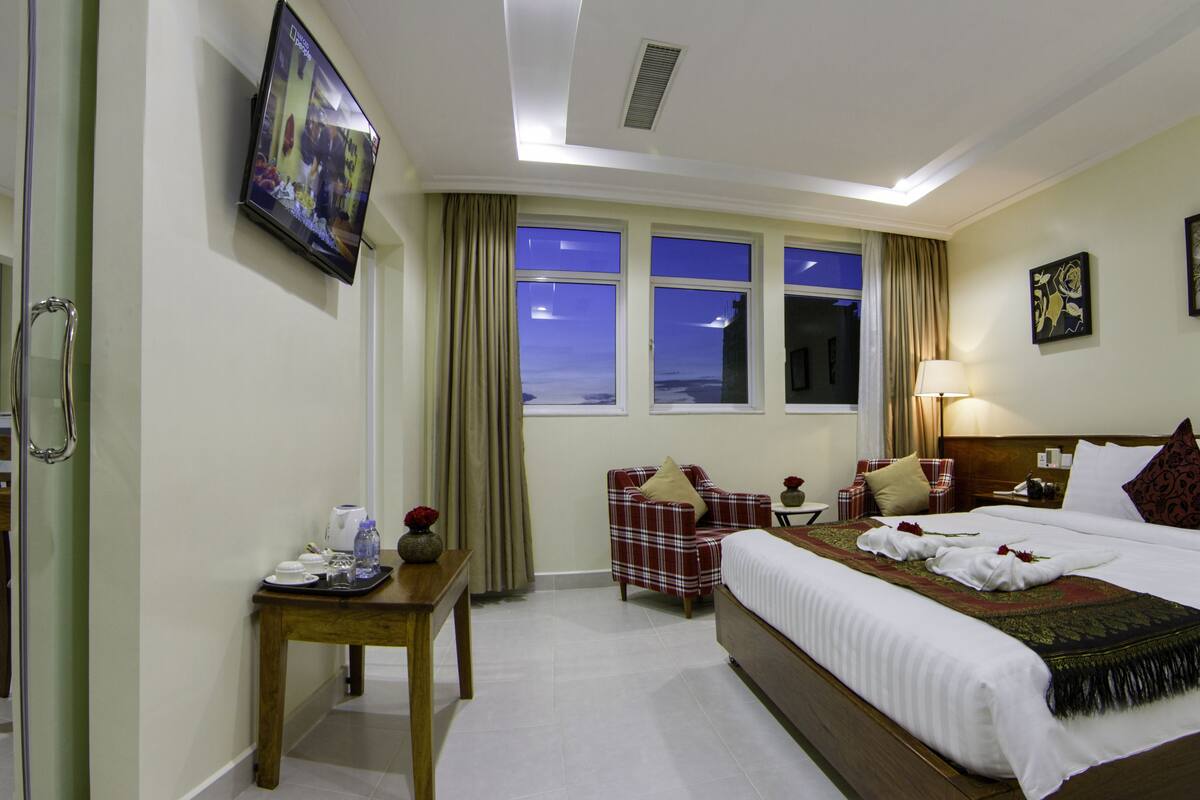 A hotel room with a bed, a TV, a desk, a chair, and a window with curtains.