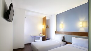 Camera d'albergo con due letti, una scrivania, una sedia, una TV e luci a parete.