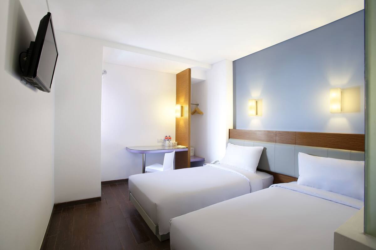 Habitación de hotel con dos camas, un escritorio, una silla, un televisor y luces fijadas a la pared.