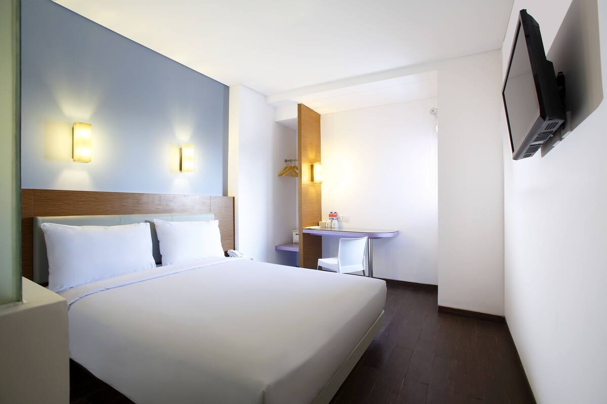 Una habitación de hotel con una cama grande, mesitas de noche, un escritorio, una silla y un televisor montado en la pared.
