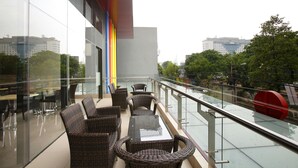 Zona relax esterna moderna con mobili in vimini e ringhiera in vetro con vista sulla città.