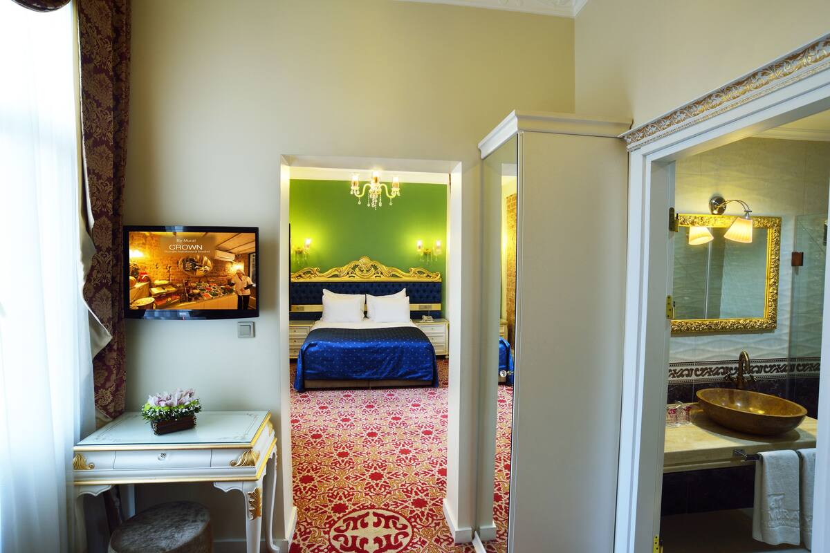 A hotel room with a bed, a desk, a mirror, and a bathroom with a sink and mirror.