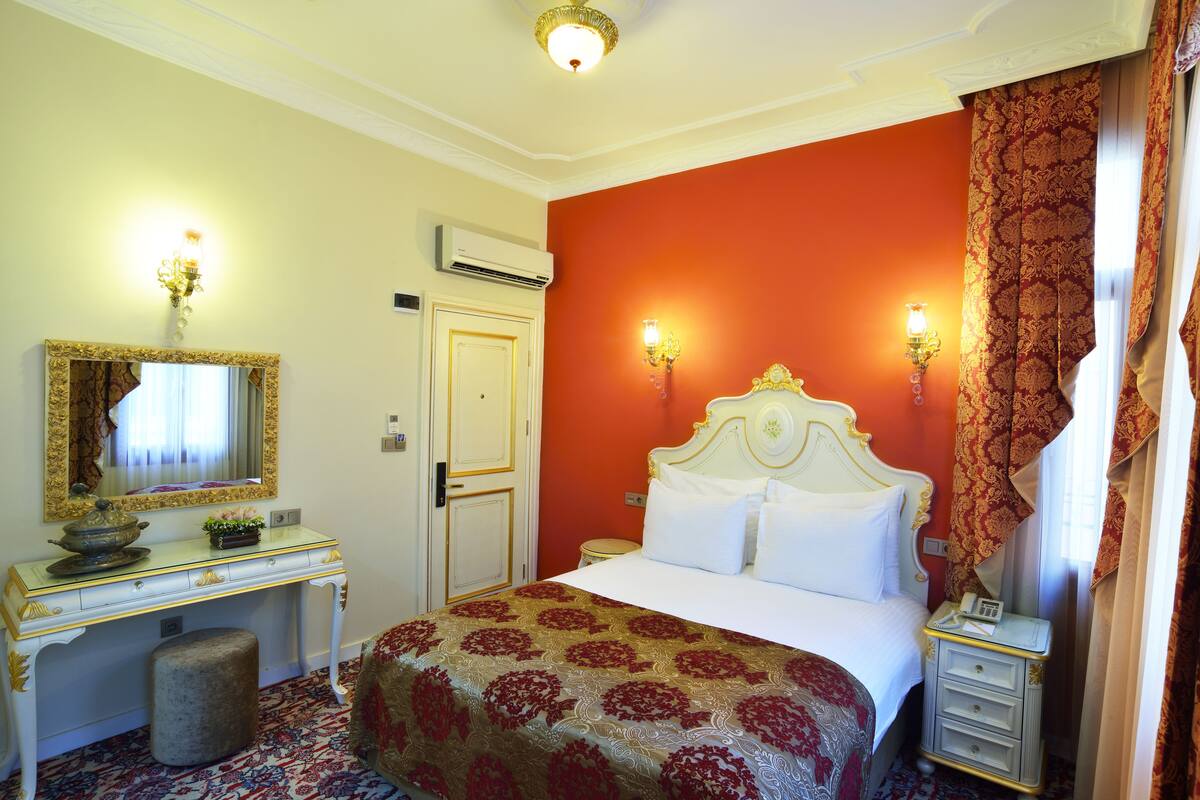A hotel room with a bed, a desk, a mirror, and two wall sconces.