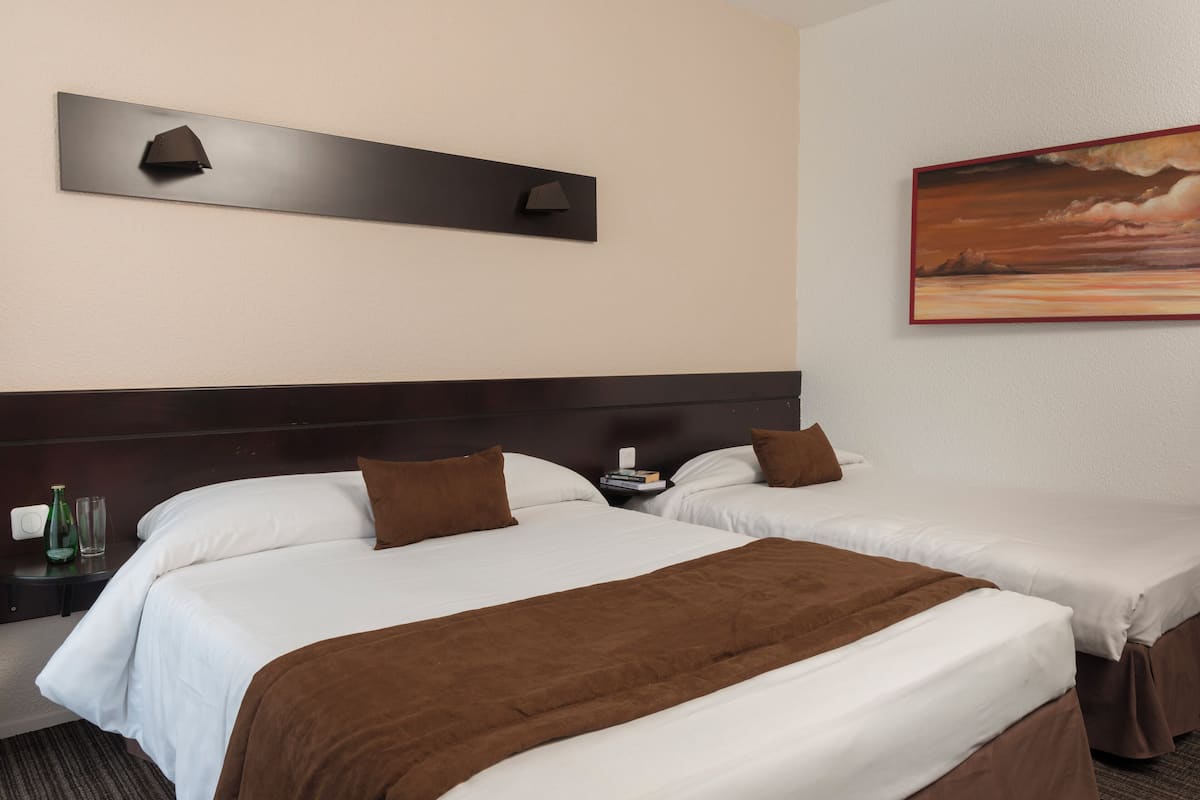 Une chambre d’hôtel avec deux lits, une table de chevet, un tableau et un luminaire fixé au mur.