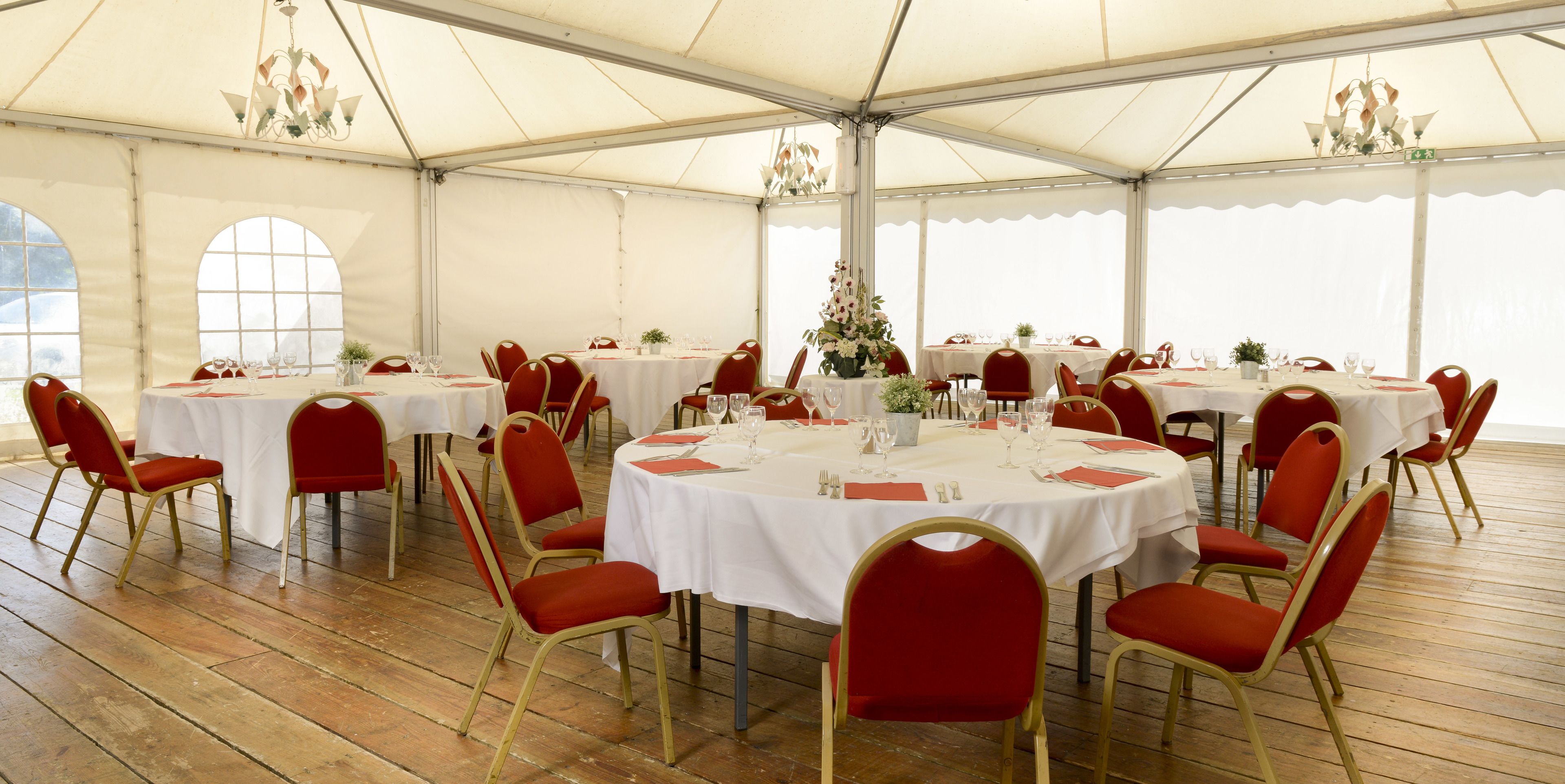 A tented dining area with round tables, red chairs, and white tablecloths.