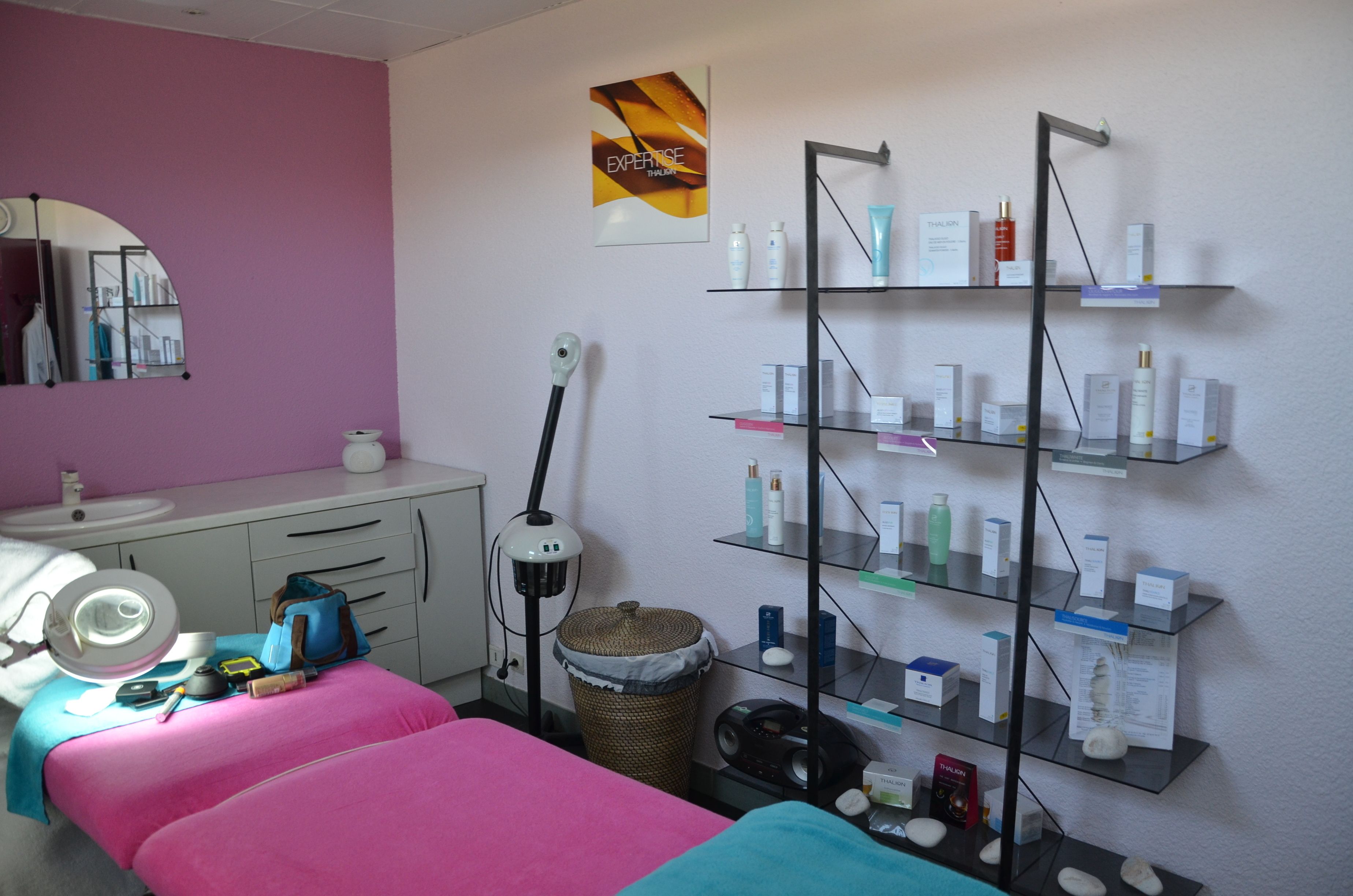 A room with a pink bed, a white sink, a mirror, and shelves with various toiletries.