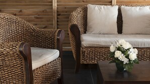 A wicker sofa with a cushion and a matching armchair, both with a light-colored cushion.