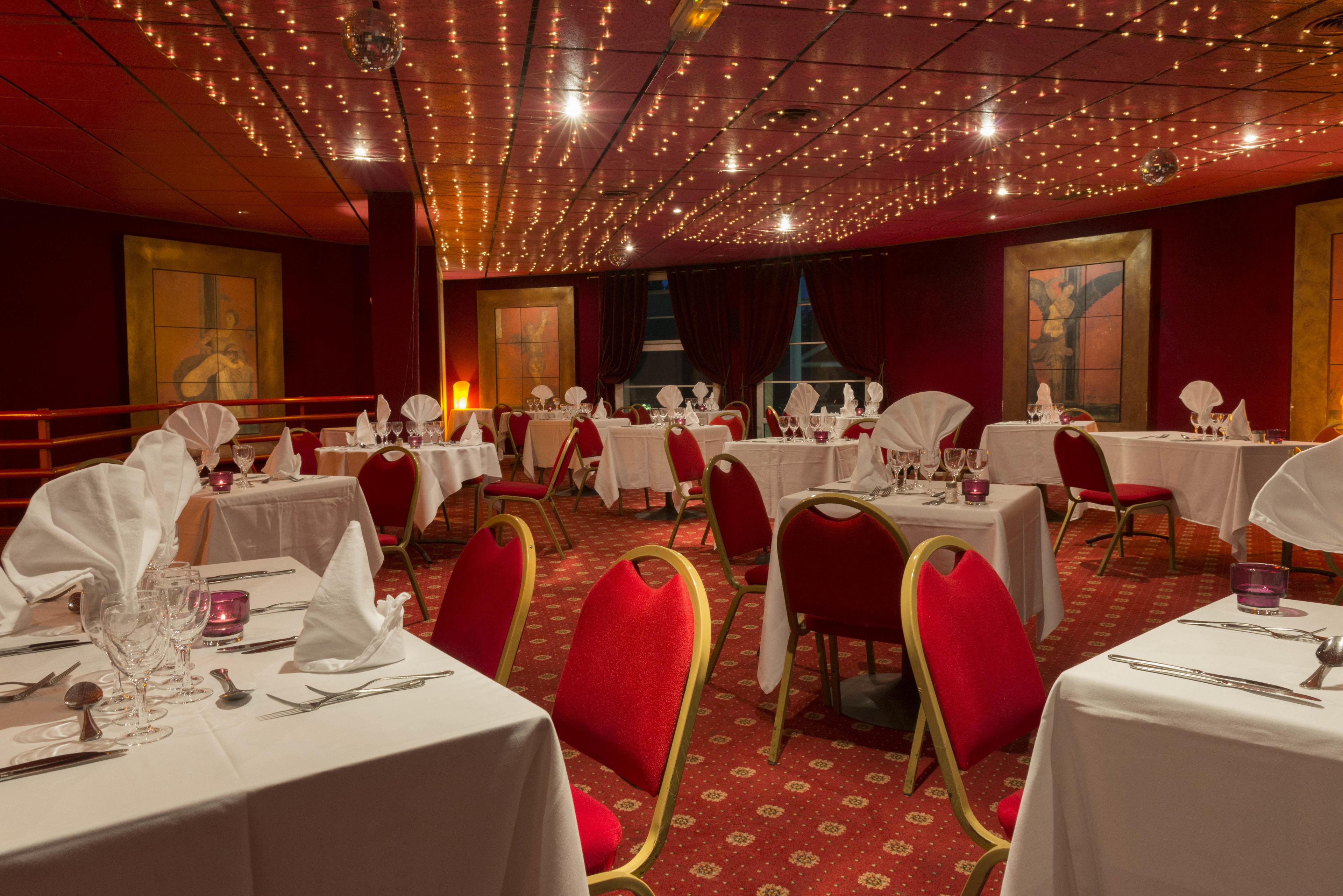 Un salón de banquetes con mesas dispuestas para comer, sillas rojas e iluminacion con luces colgantes.