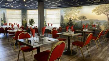 A restaurant with red chairs and tables, large windows with blinds, and a mural of a landscape.