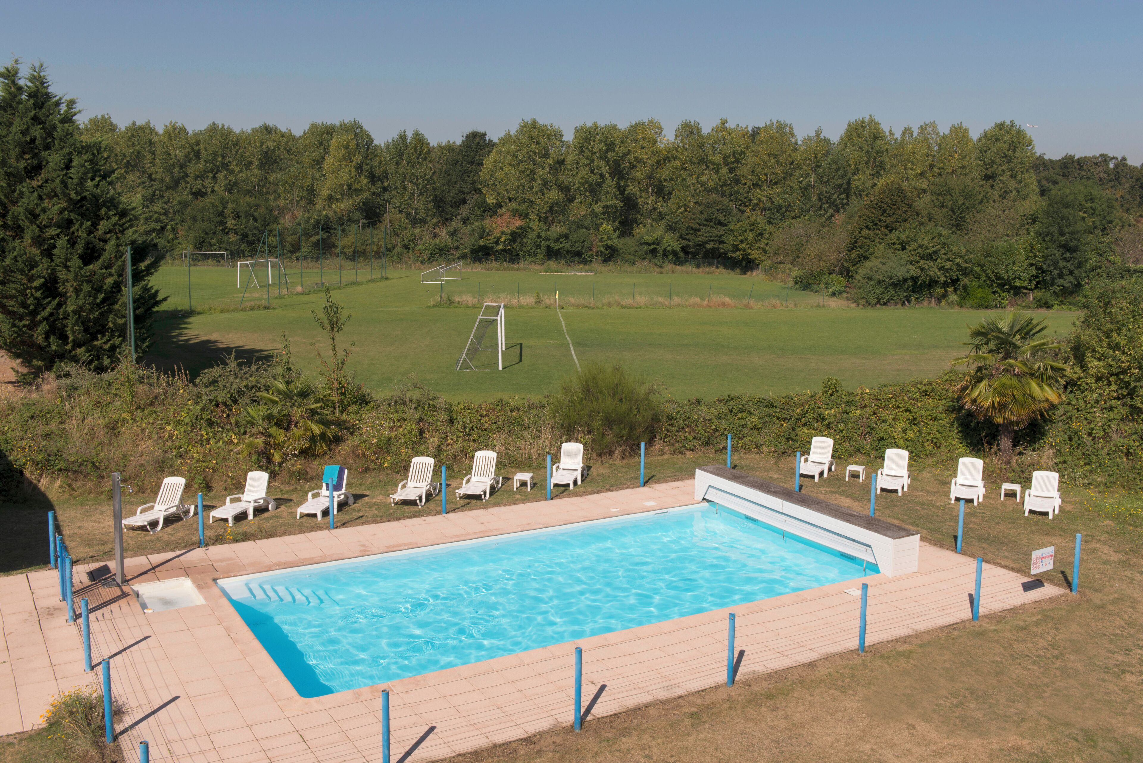 A swimming pool with a view of a soccer field and trees in the background.